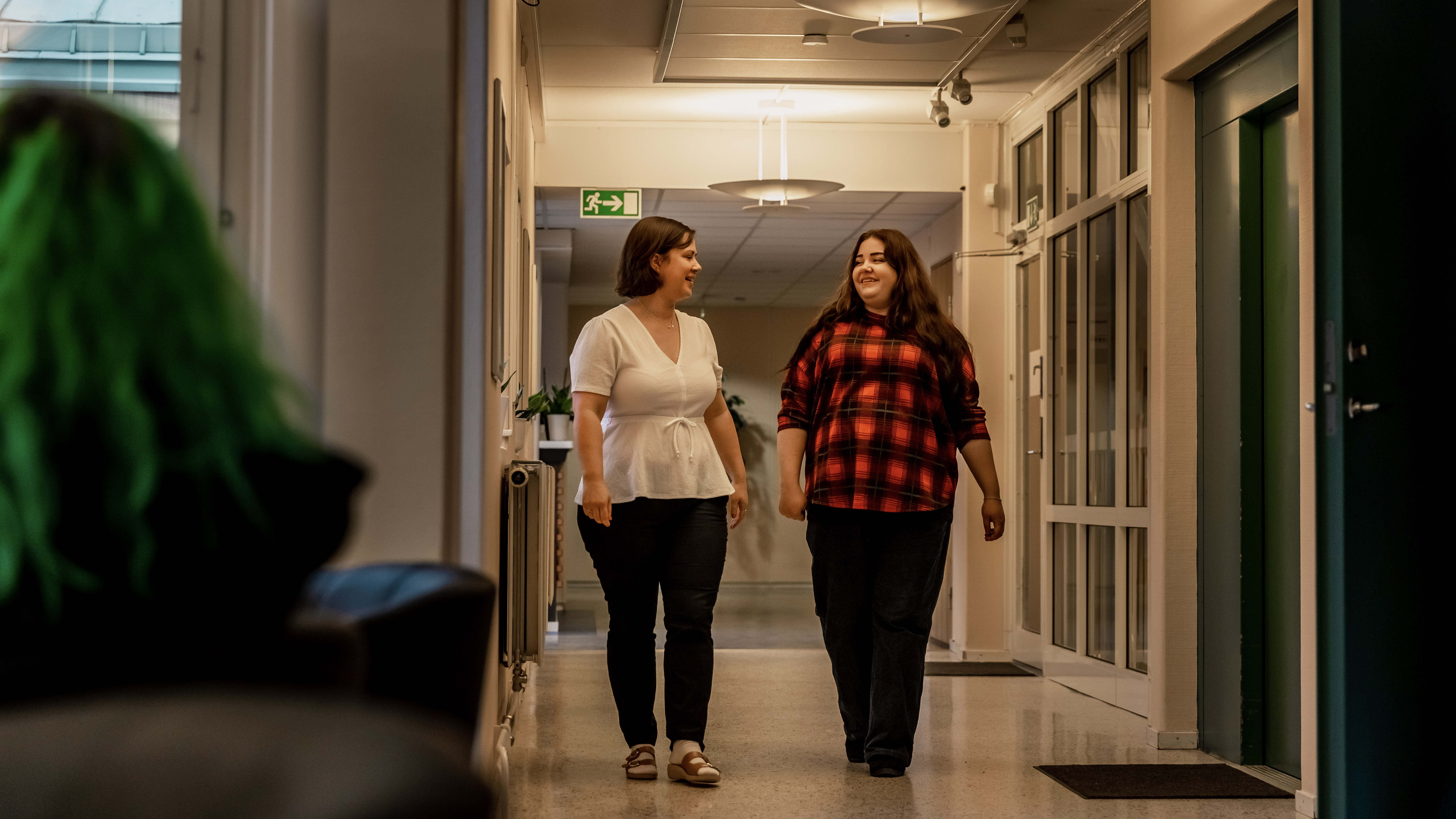 Två kvinnor samtalar gåendes i en korridor